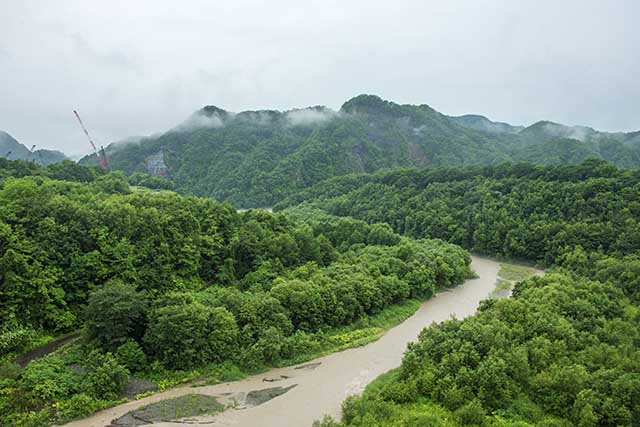 額平川の支流宿主別川の橋の上から平取ダム建設現場を見る。正面の山が神聖な山「チノミシリ」である。
